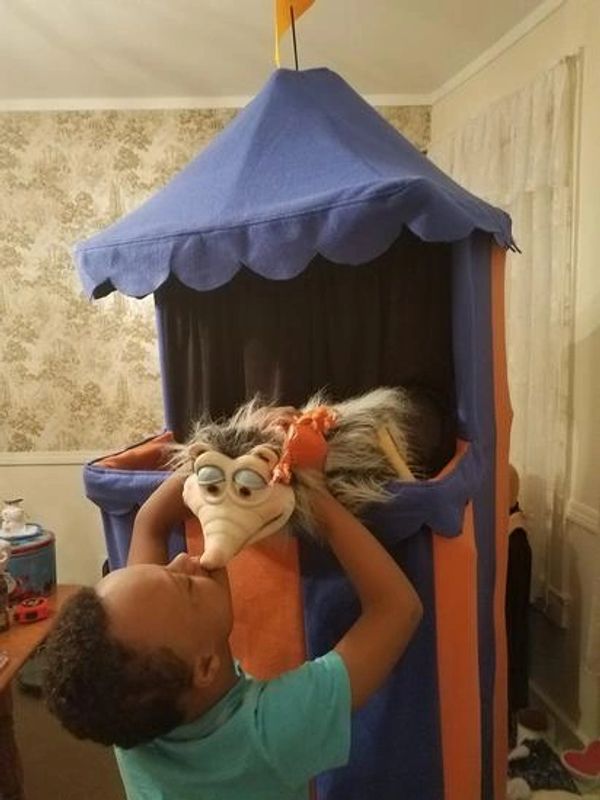 Child interacting with puppet inside blue and orange play tent